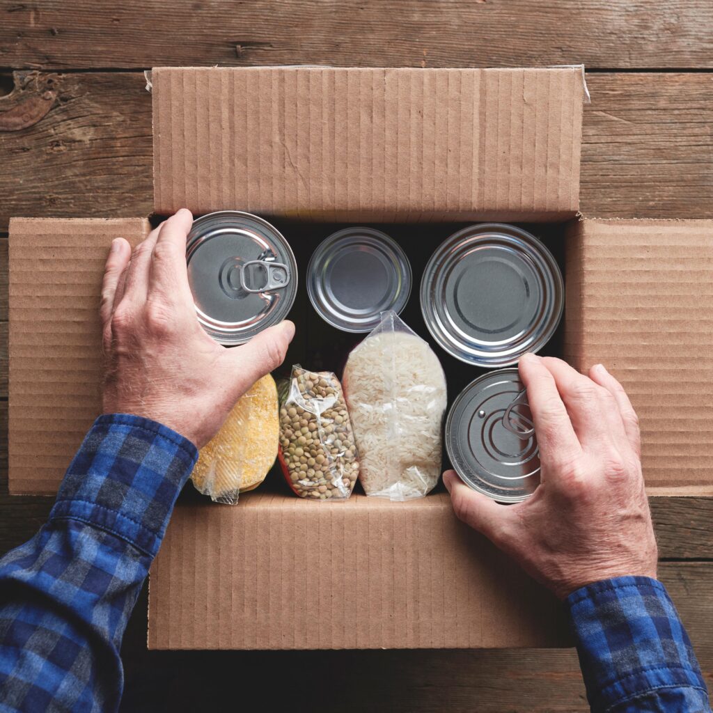 Hands filling a cardboard box with food items.